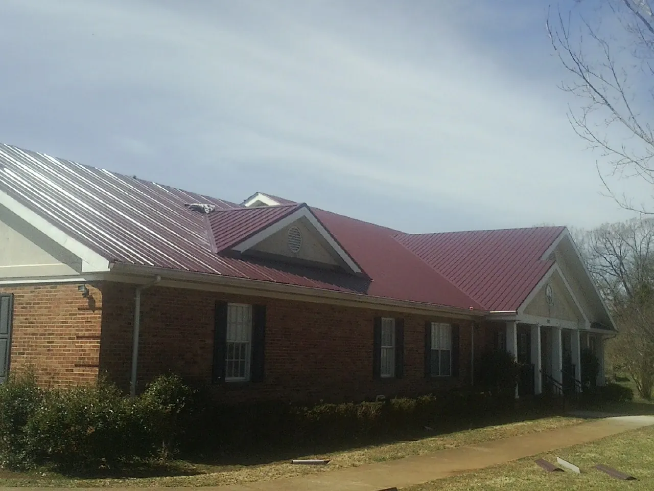 Red metal roof with gabled entries on a long brick building, from a Hail Damage Roof Repair job in Beaver Springs