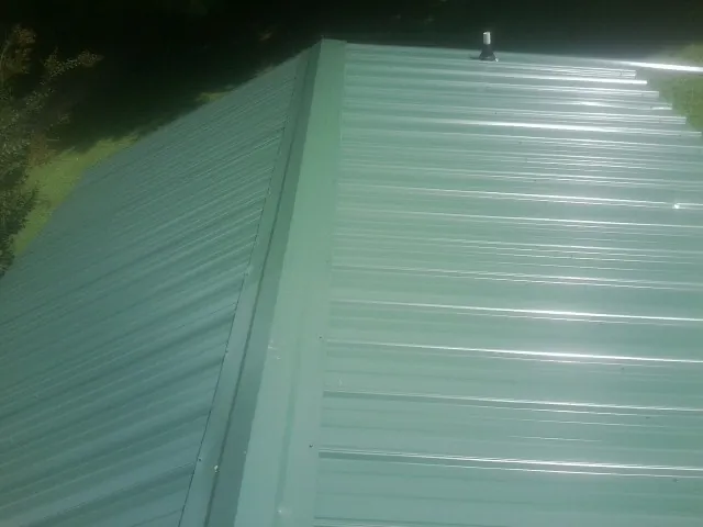 New green metal panels meeting at the ridge of a roof — Flat Roof Repair work by our crew in Beaver Springs