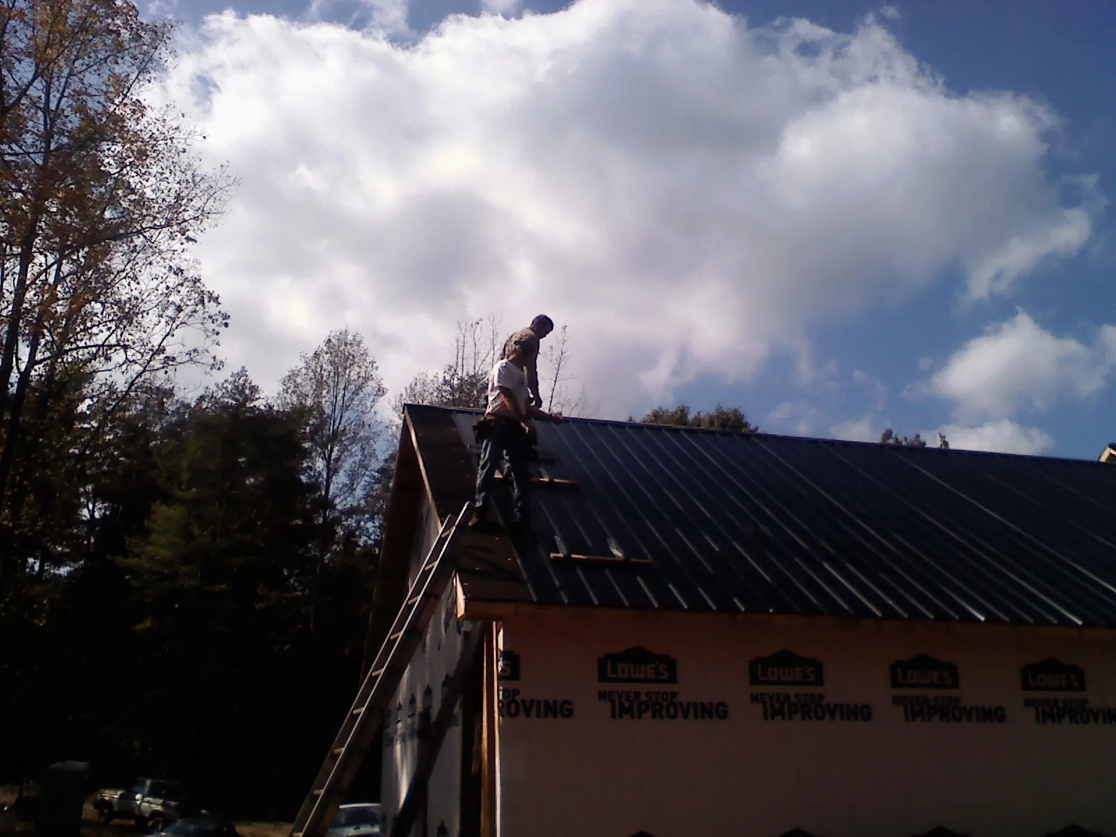 Roofer fastening dark metal panels high against a cloudy sky, from a Roof Inspection job in Beaver Springs