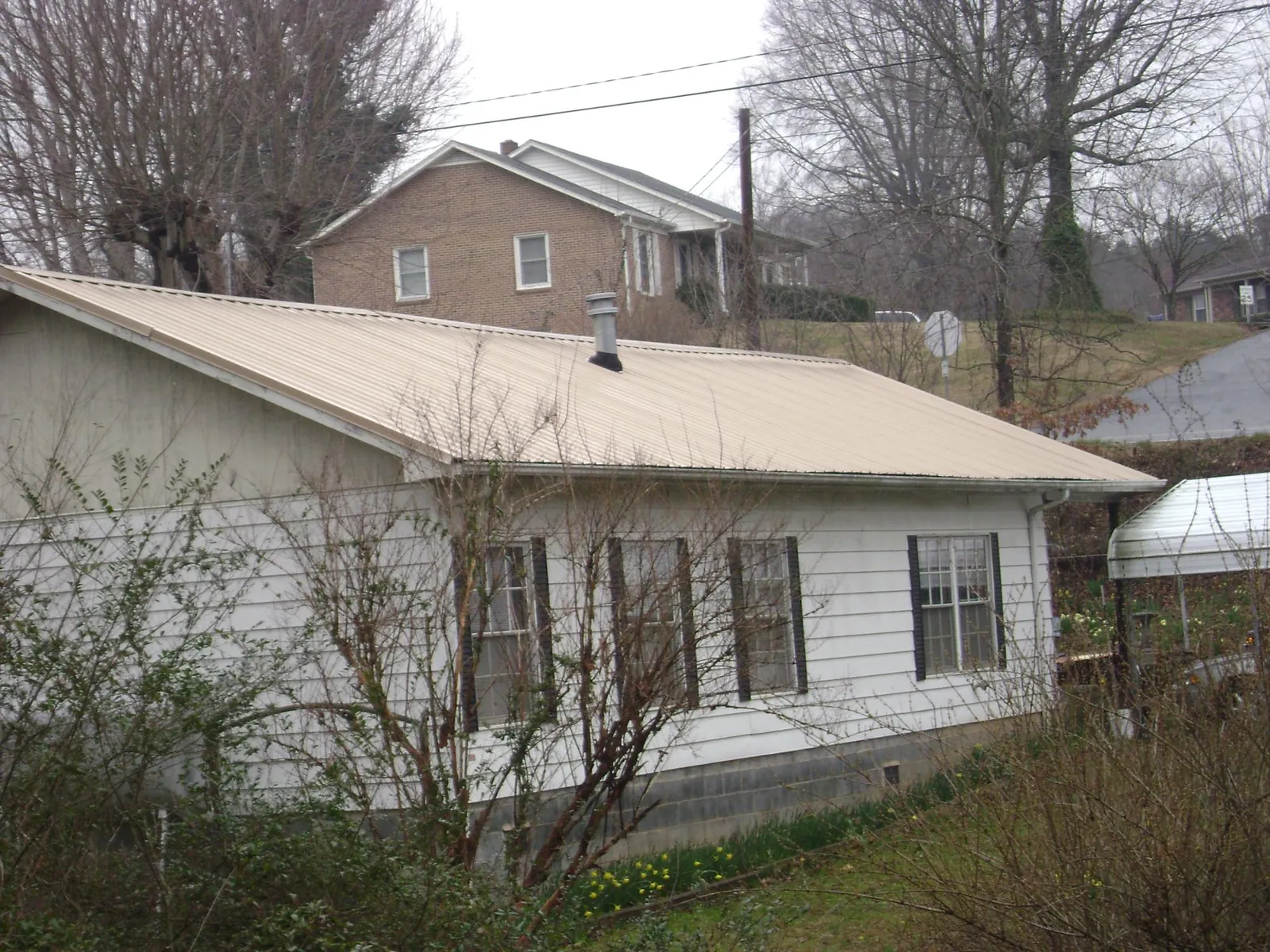 Tan metal roof on a white sided house set into a hillside — Commercial Roofing by Roofing Brothers in Beaver Springs